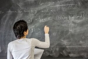 A female math professor writes equations on a chalkboard.