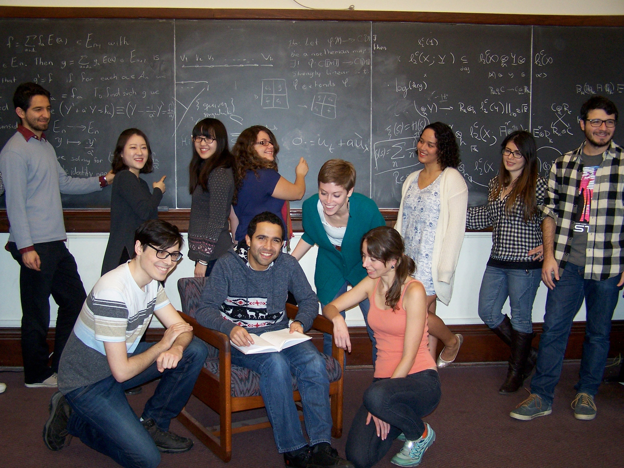 Smiling graduate students posed in front of a chalkboard with mathematics.