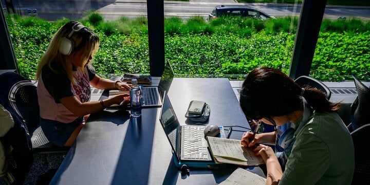 Students studying at table with laptops and notebooks.