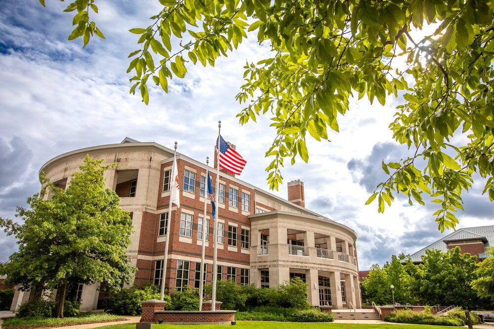 Image of the Alice Cambell Alumni Center during the day in spring. The building is surrounded by green trees.