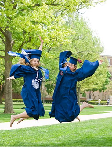 Graduates dressed in blue regalia jump with joy on campus quad.