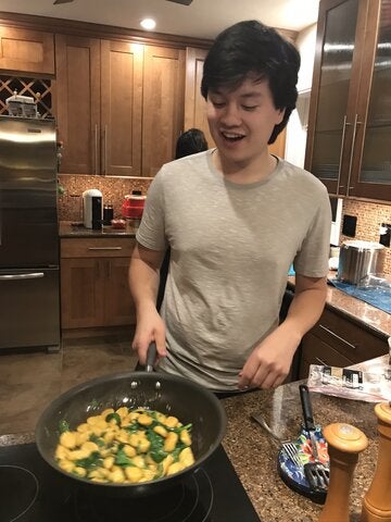 Reed Oei stands in the kitchen, sauteeing food in a skillet. 