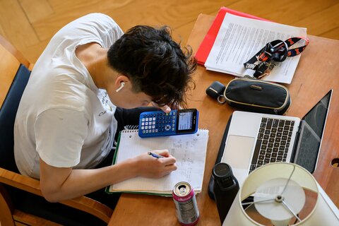 A student uses a calculator while writing in a notebook.