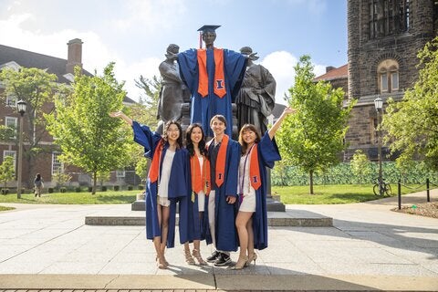 Students in graduation regalia pose in front of the Alma Mater statue on University of Illinois campus