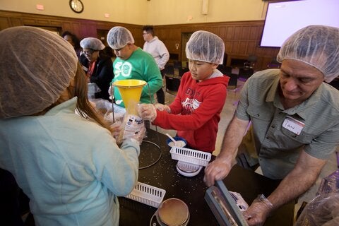 People wearing gloves and hairnets weigh and sort food into containers.