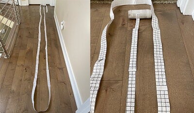 A long strip of paper is lain across a wooden floor. Handwritten numbers appear on the strip of paper.