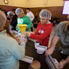 People wearing gloves and hairnets weigh and sort food into containers.