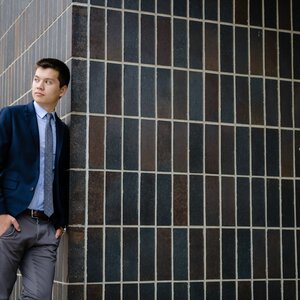 Reed Oei stands near a black tiled wall. 