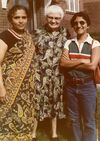 Three women pose for a photo. The woman on the left is wearing a black blouse and colorful sari. The woman in the middle is wearing a paisley print dress. The woman on the right is wearing a striped polo shirt, blue jean, and sunglasses. 